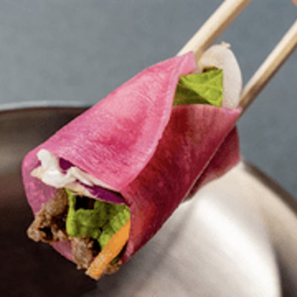 Pink wrap filled with meat, lettuce, and vegetables, held by chopsticks.