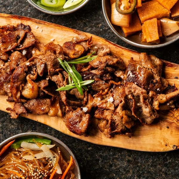 Grilled meat with green onions on a wooden board, served with pickled vegetables and glass noodles.